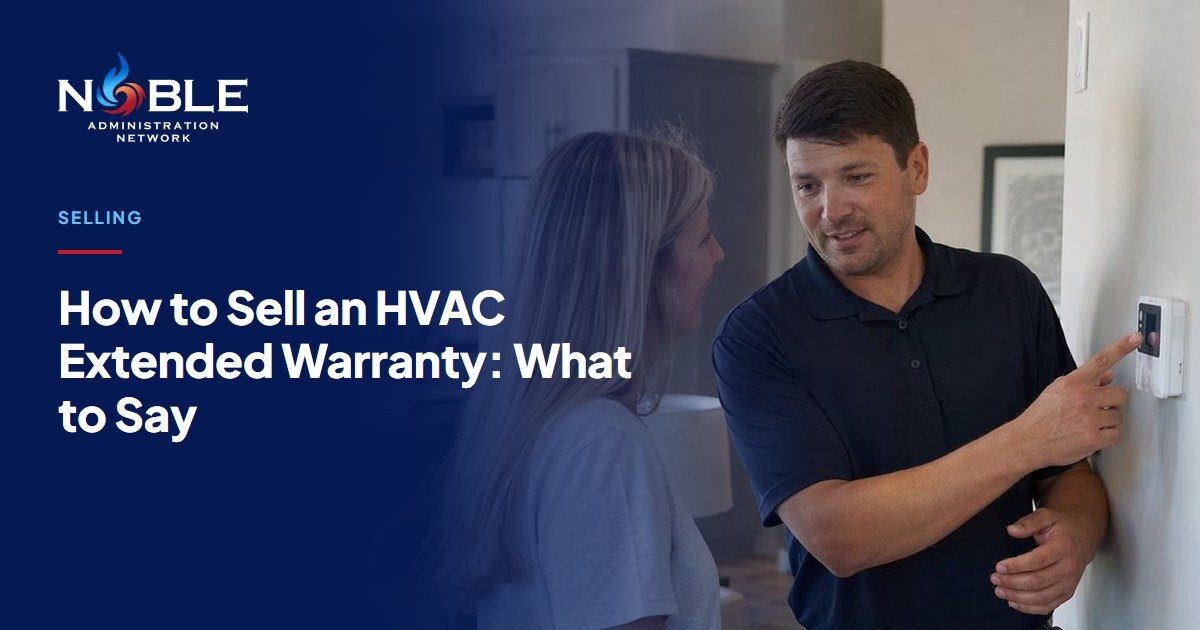 An HVAC technician in a navy polo points to a wall thermostat while explaining it to a homeowner in her kitchen.